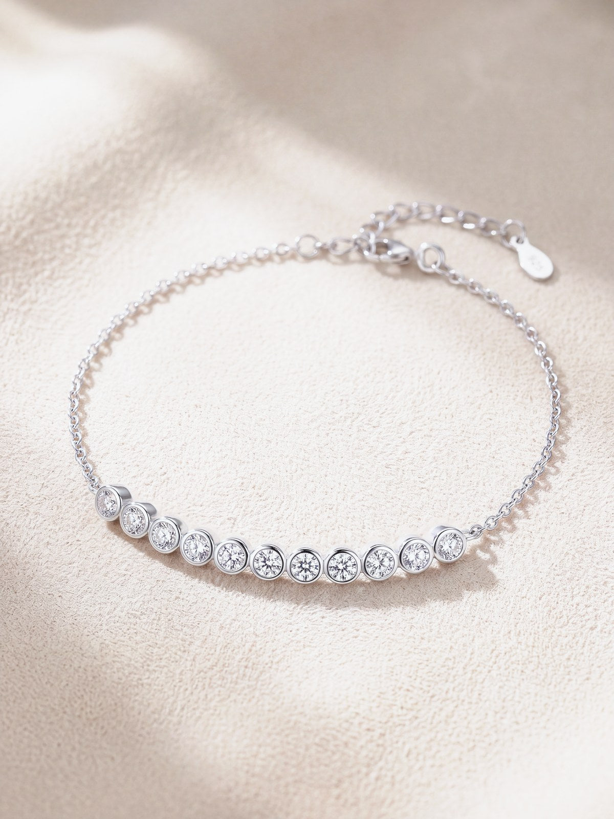Silver moissanite bracelet with graduated bezel-set stones on cream suede
