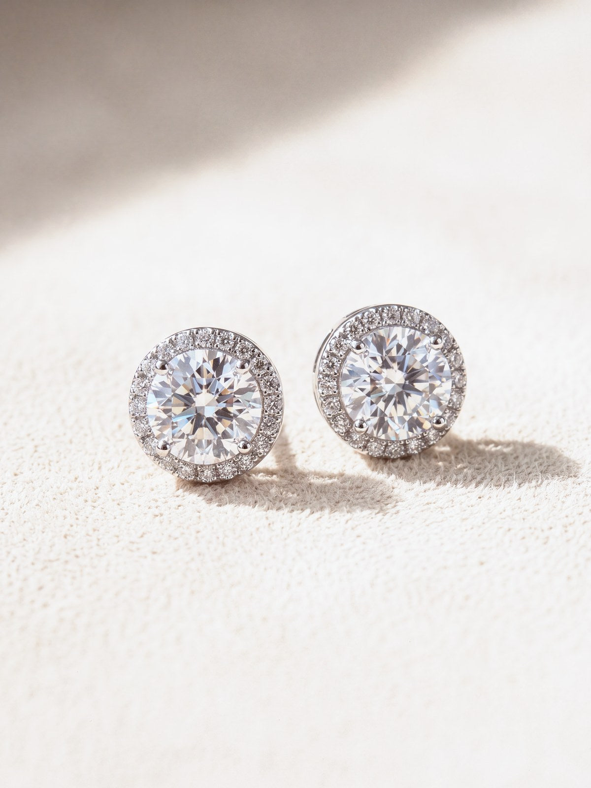 Pair of silver moissanite halo stud earrings on cream suede