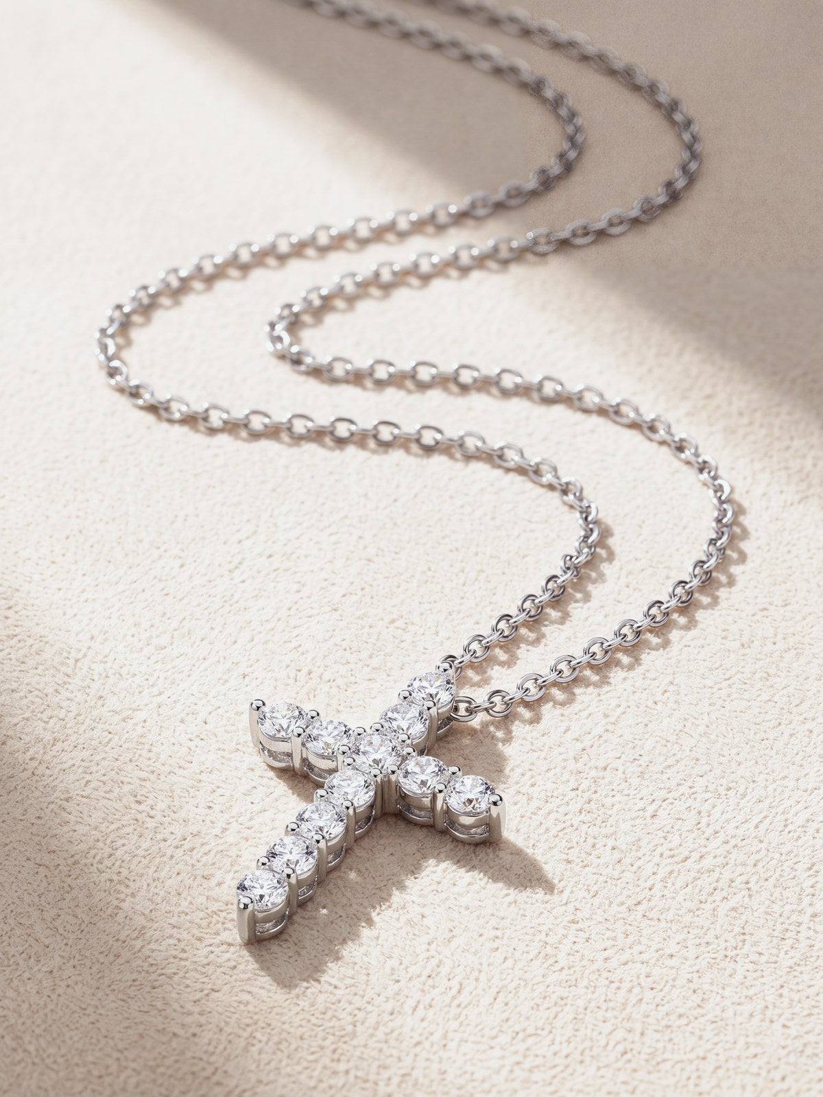 Silver moissanite cross pendant and chain laid out on cream suede