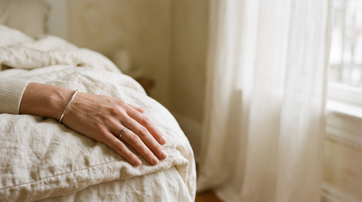 A hand resting on cream linen wearing a silver moissanite solitaire ring in morning light